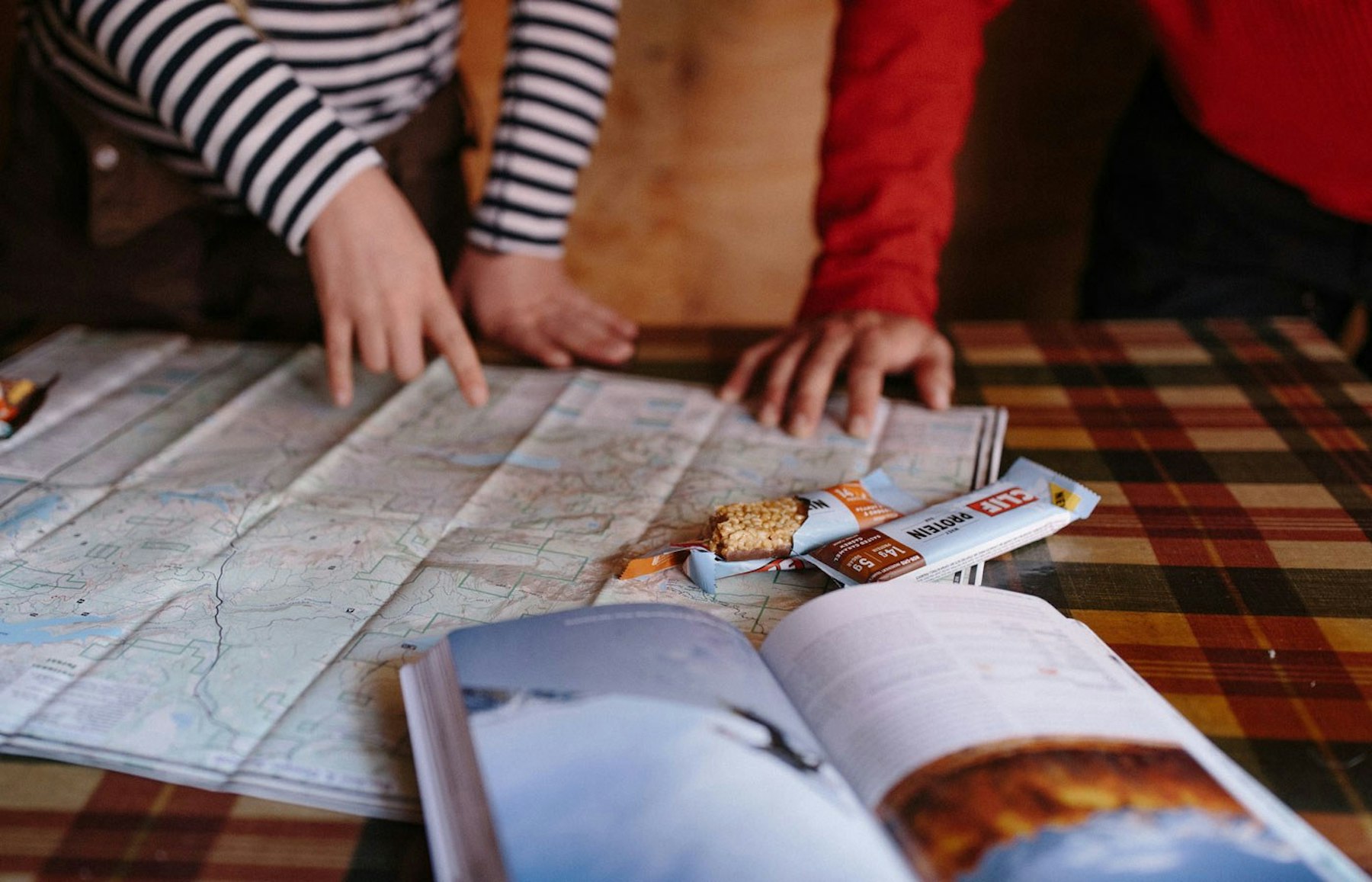 Hands pointing at a map on a table - protein bars on table